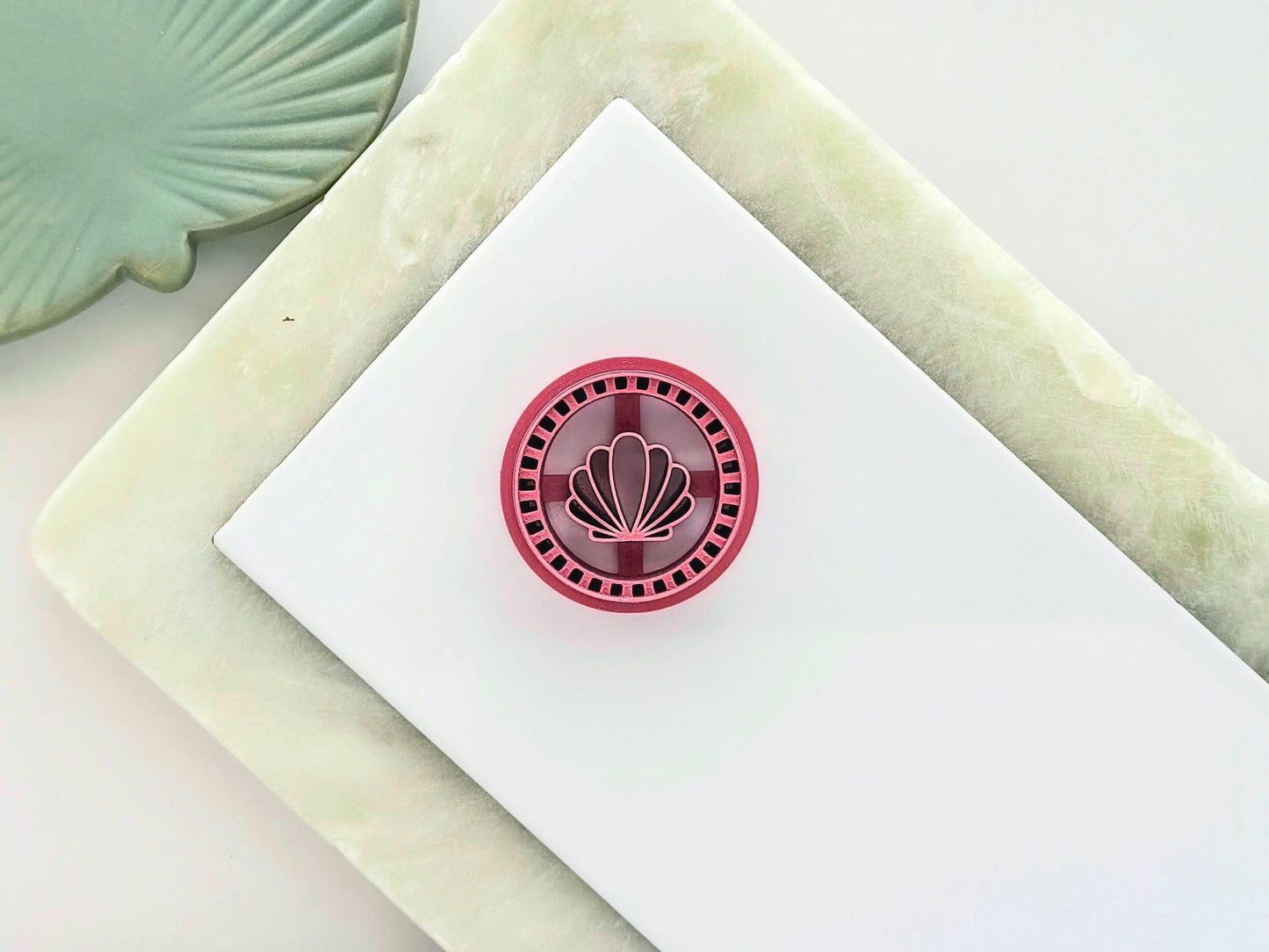 Pink circle clay cutter on a white tile with clam shell central stamp detail in a frame style