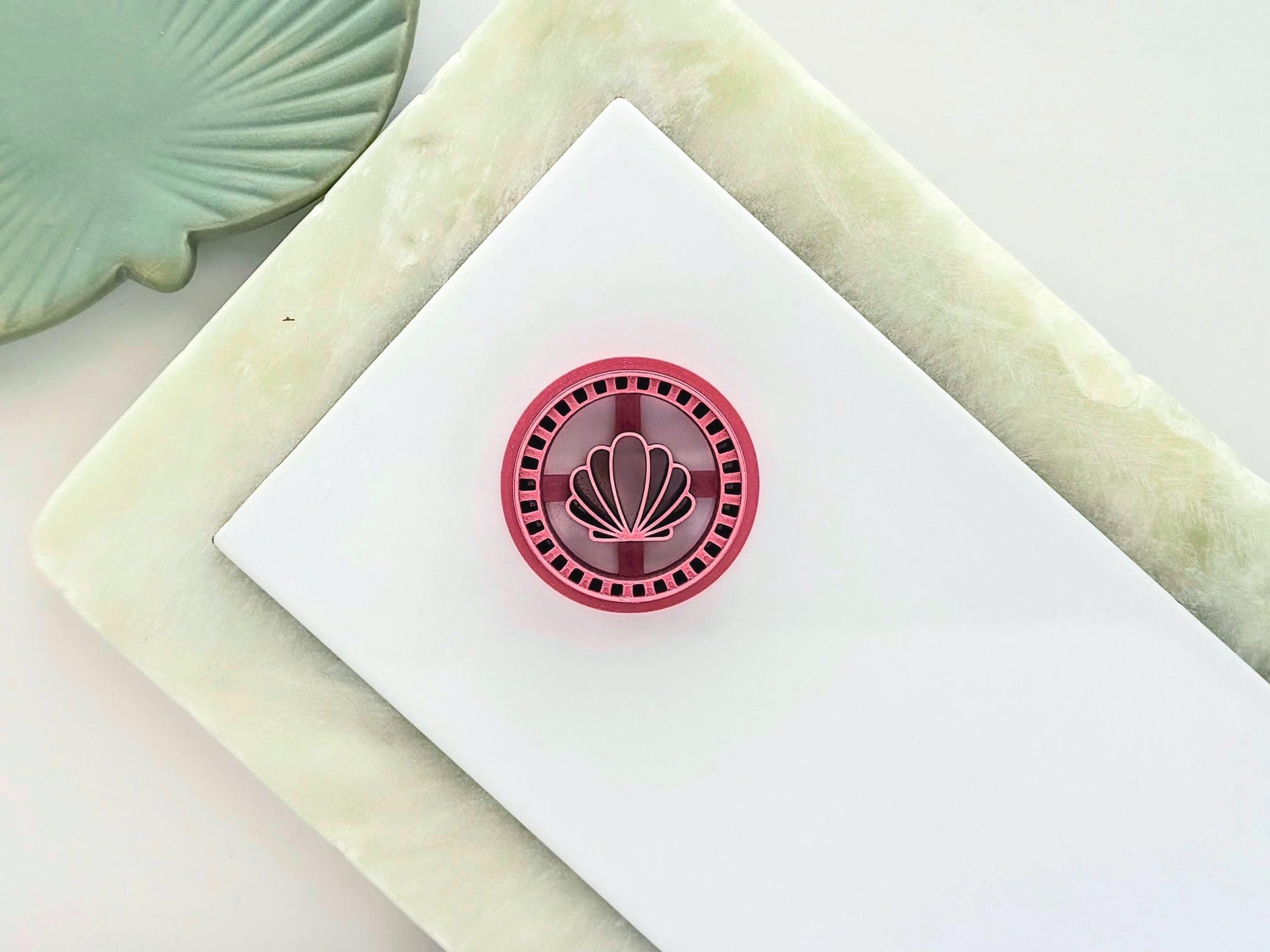 Pink circle clay cutter on a white tile with clam shell central stamp detail in a frame style