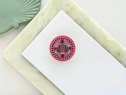 Pink circle clay cutter on a white tile with clam shell central stamp detail in a frame style
