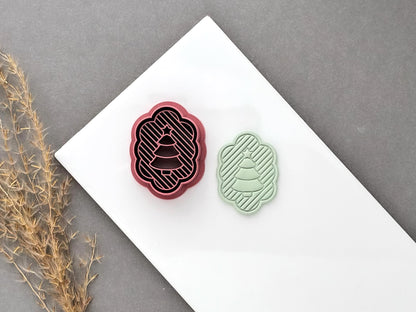 Christmas tree polymer clay cutter displayed beside a matching finished clay cut-out, featuring a scalloped oval frame, striped background and layered Christmas tree design.