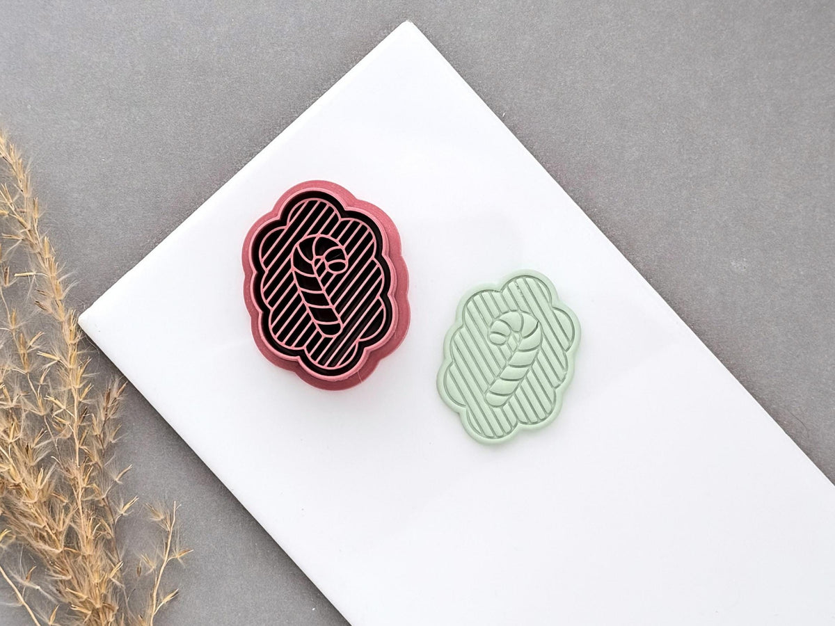 Christmas candy cane polymer clay cutter displayed beside a matching finished clay cut-out, featuring a scalloped frame, striped background and central candy cane design.