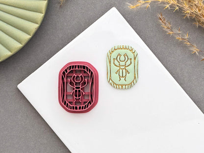 Scarab beetle polymer clay cutter displayed beside a matching finished polymer clay embellishment featuring a detailed scarab beetle within a decorative Egyptian-inspired border.