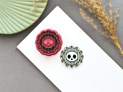Skull cameo polymer clay cutter displayed alongside a finished polymer clay skull cameo sample, featuring a decorative ornate frame with striped background for creating gothic jewellery, Halloween charms and spooky craft projects.