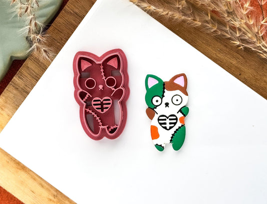 Halloween clay cutter in the shape of a zombie cat with paws up. Includes heart shaped ribs and stitching stamp details.