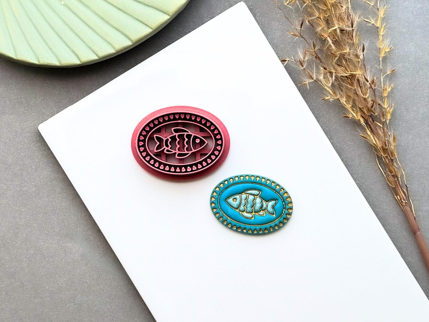 Fish polymer clay cutter displayed alongside a finished polymer clay fish sample, featuring an oval beaded frame with intricate fish embossing for creating coastal jewellery, ocean-inspired charms and marine craft projects.