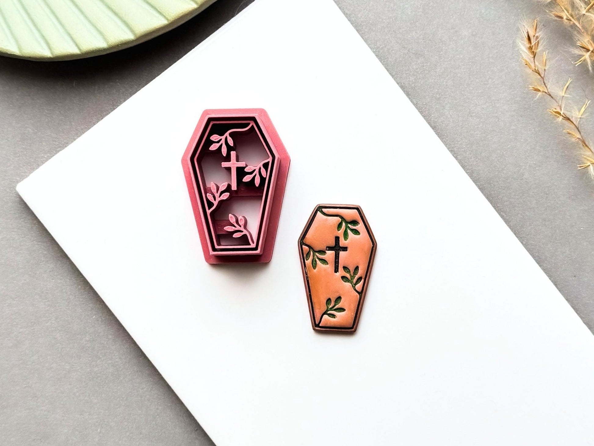 Coffin-shaped polymer clay cutter displayed beside a matching finished clay embellishment, featuring a cross and delicate botanical details, perfect for gothic, Halloween, alternative and dark botanical clay projects.