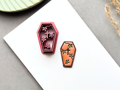 Coffin-shaped polymer clay cutter displayed beside a matching finished clay embellishment, featuring a cross and delicate botanical details, perfect for gothic, Halloween, alternative and dark botanical clay projects.