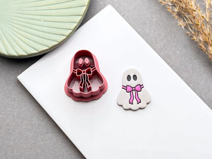 Angled view of a cute ghost bow polymer clay cutter beside a finished polymer clay ghost earring.