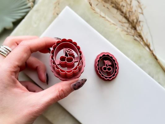 Side view of summer style cherry polymer clay earring cutter. The clay cutter is being held in a hand to show sharp cutting edge and imprint depth.