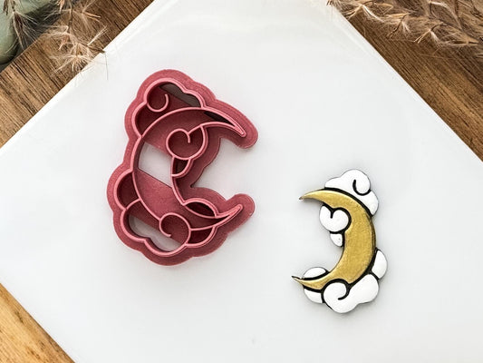 Moon and clouds shaped polymer clay cutter in dark pink on a white tile
