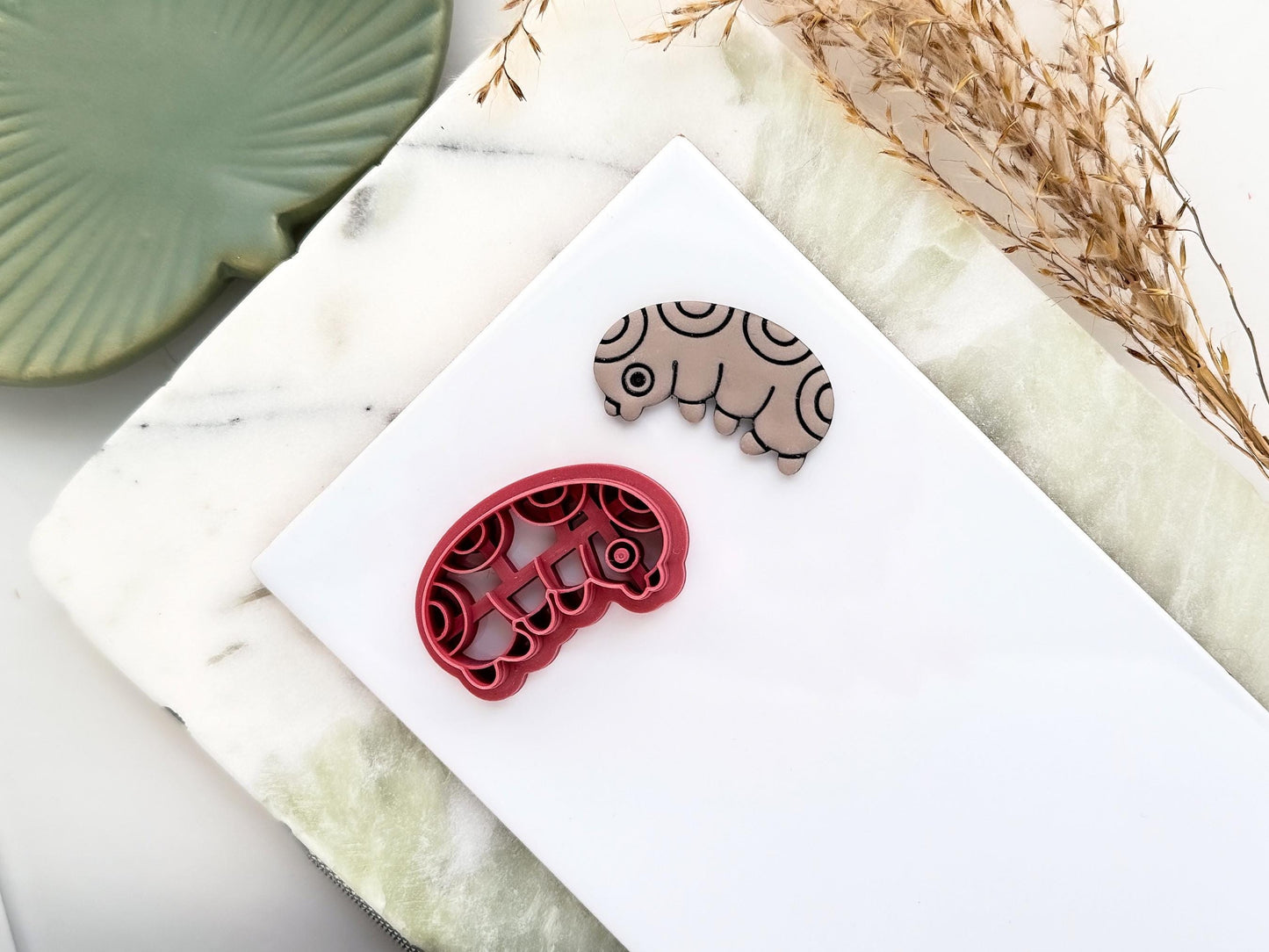 Gub bug shaped clay cutter with circle pattern. Next to the cutter is a polymer clay cut out sample earring