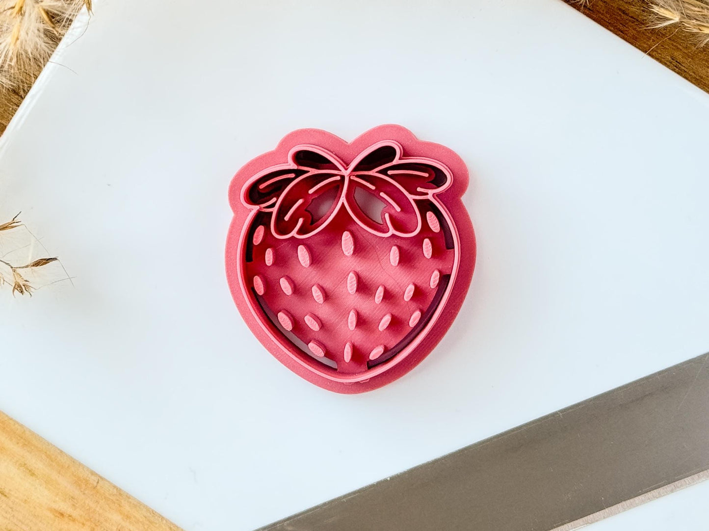 pink strawberry shaped clay cutter with pip and leaf details on a white tile