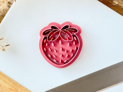 pink strawberry shaped clay cutter with pip and leaf details on a white tile