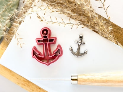 Anchor shaped polymer clay cutter i pink with silver coloured clay cut out sample. Both lying on a white tile