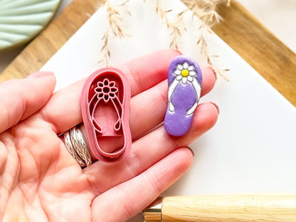 Summer sandle clay cutter with cut out shape showing straps and flower details being held in a hand for scale