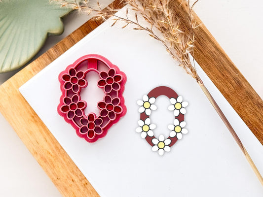 Oval polymer clay cutter with 5 daisy stamped shapes around a ring.