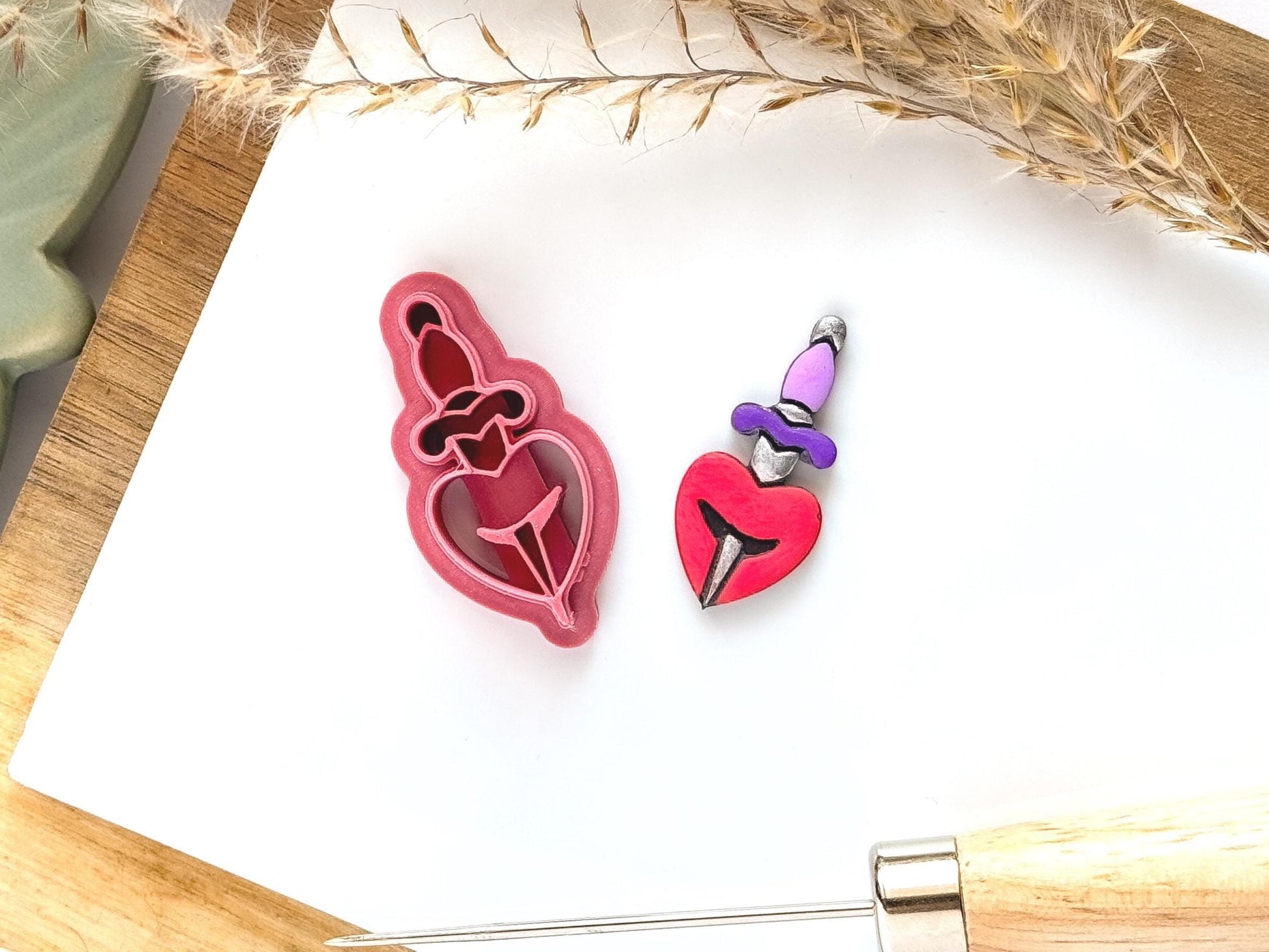 Heart and dagger clay cutter shape on a white tile with a painted polymer clay cut out