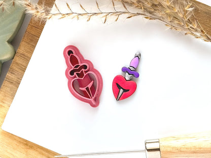 Heart and dagger clay cutter shape on a white tile with a painted polymer clay cut out