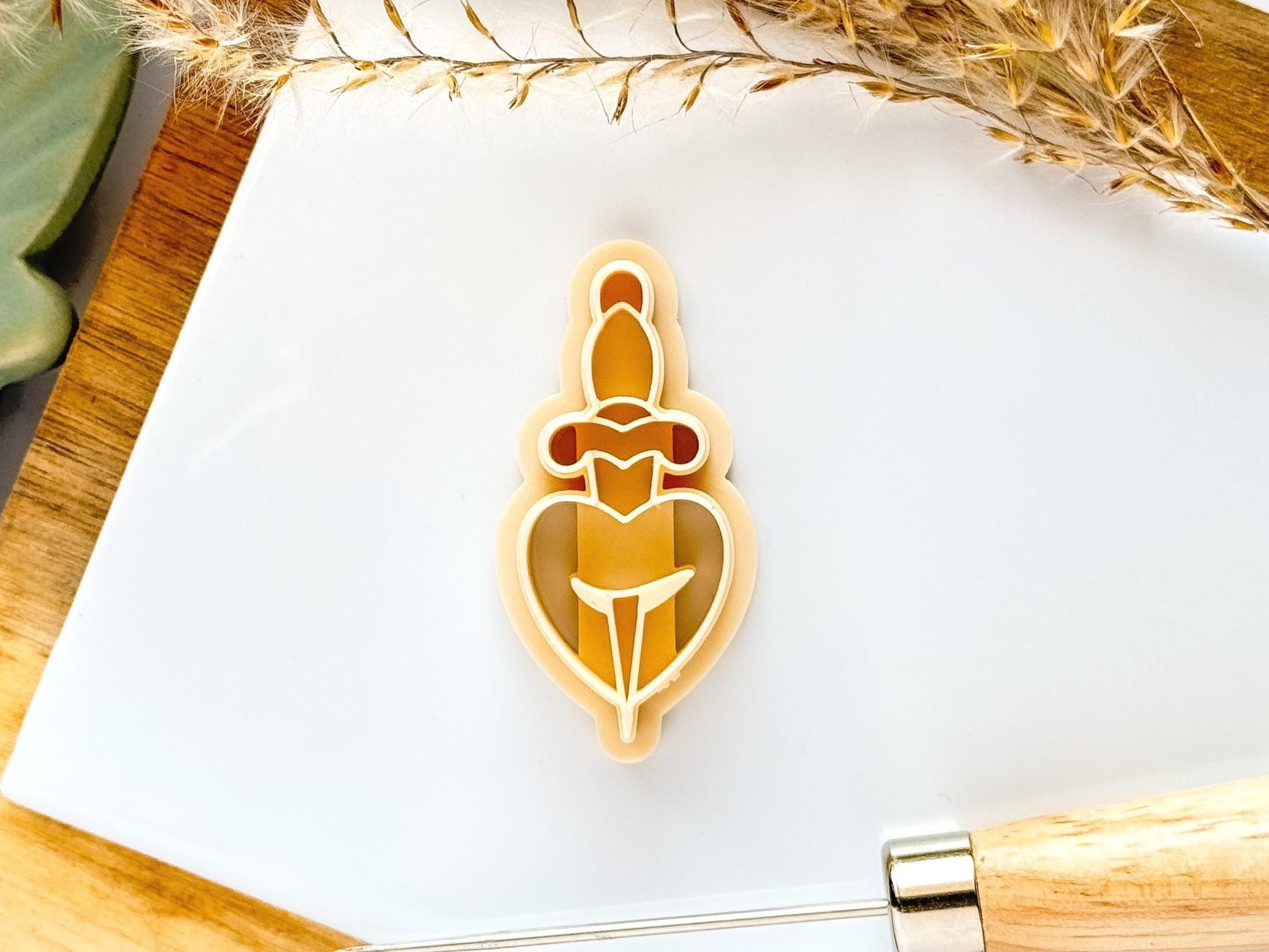 Beige coloured beytrayed heart polymer and silver clay cutter on a white tile