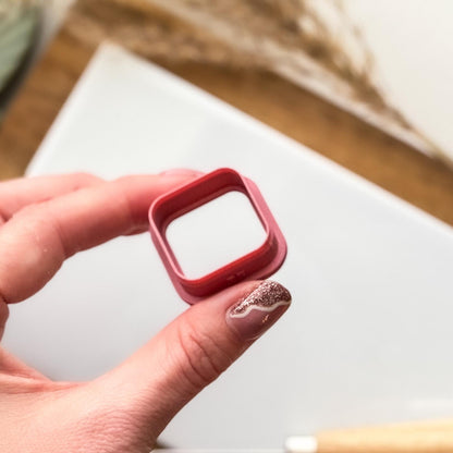 Tilted side view of a rounded corner square clay cutter being held