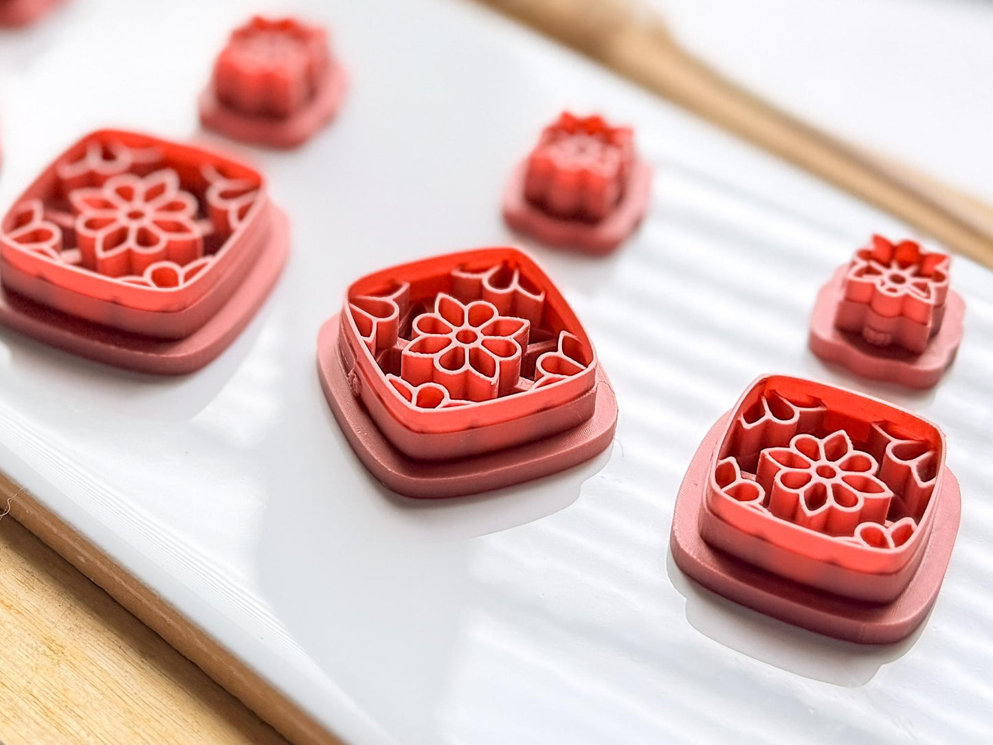 Side view of three clay earring cutters featuring a symmetical flower stamp design within a square shape and a small flower shaped stud cutter
