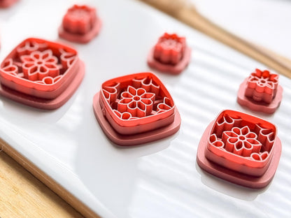 Side view of three clay earring cutters featuring a symmetical flower stamp design within a square shape and a small flower shaped stud cutter