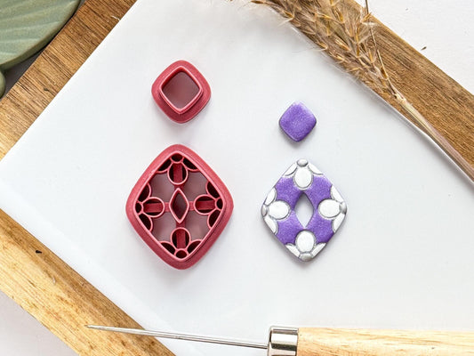 Clay earring cutter set in diamond donut shape with 4 flower stamps on the inside. To the side is a polymer clay sample piece that has been painted in white to highlight the flowers.