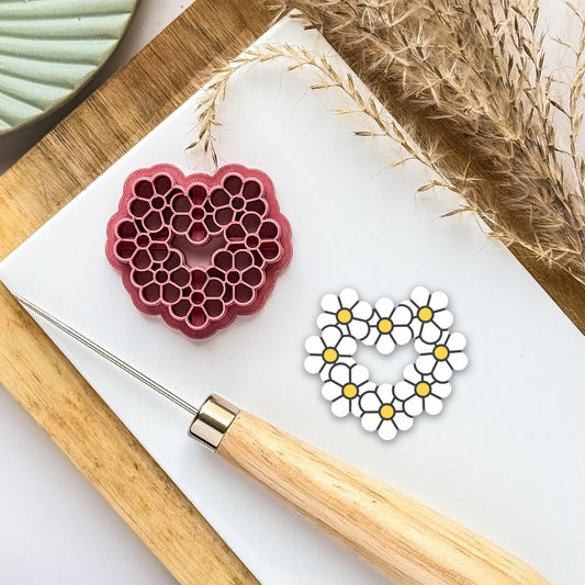 heart shaped polymer clay cutter in dark pink with simple daisy imprint patterns all the way around to form a heart made of flowers.