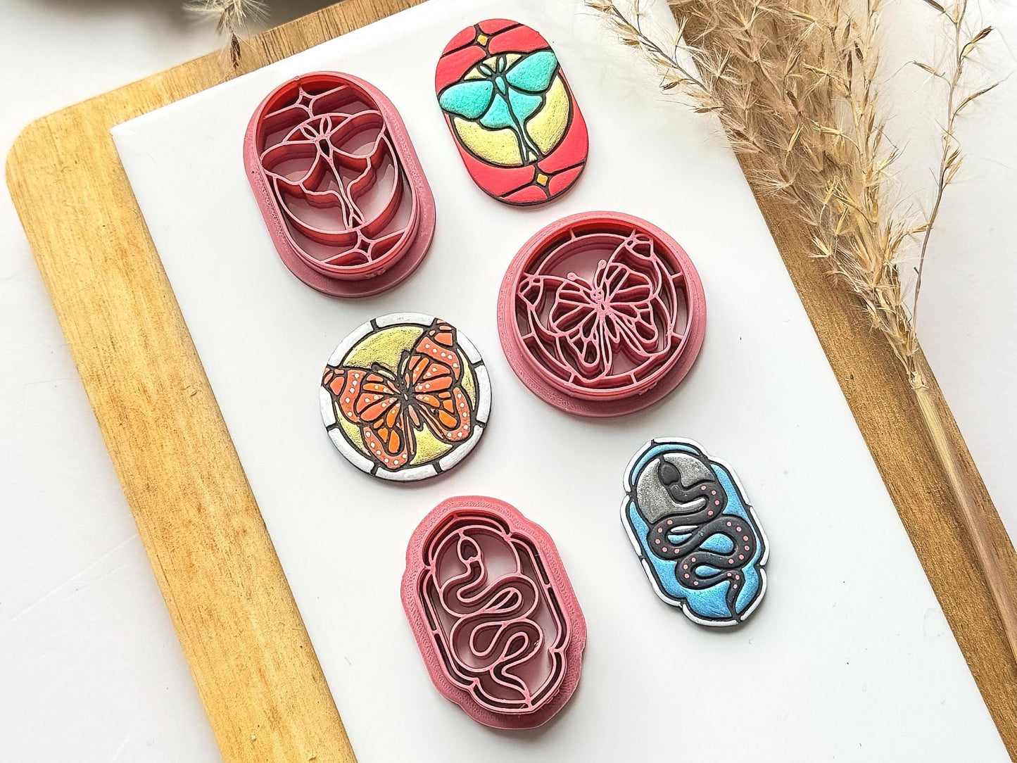 Image shows 3 stained glass effect clay cutters featuring a moth, snake and butterfly. Next to the polymer clay cutters are painted clay samples.