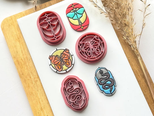 Image shows 3 stained glass effect clay cutters featuring a moth, snake and butterfly. Next to the polymer clay cutters are painted clay samples.