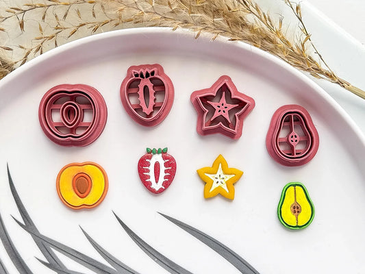 Set of four fruit shaped clay cutters in pink including a halved peach, strawberry, star fruit and pear. Below are polymer clay samples created with the cutters and painted with acrylic paint.