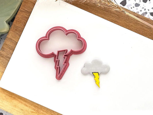 Thunder cloud shaped polymer clay cutter with lightening bolt imprint detail. Example shape made from grey polymer clay is located next to it.