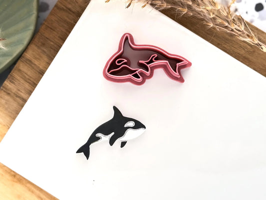 3d printed Orca or killer whale shaped clay cutter in dark pink with painted polymer clay sample shape.