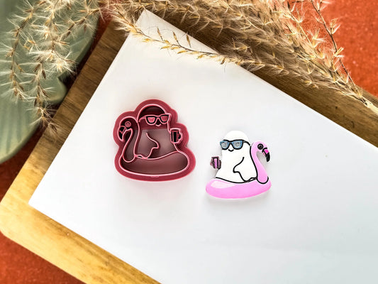 Pool party ghost clay cutter, ghost is sitting in a flamingo shaped floatie wearing sunglasses and holding a drink.
