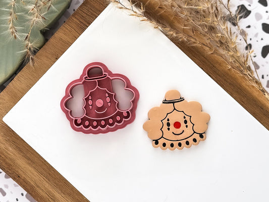 Pink cute happy clown shaped clay cutting tool for circus themed clay and baking projects next to a polymer clay sample piece.