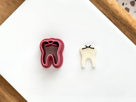Craft cutter in the shape of a molar tooth with bite details and tooth root, with a polymer clay sample cut out shape next to it.
