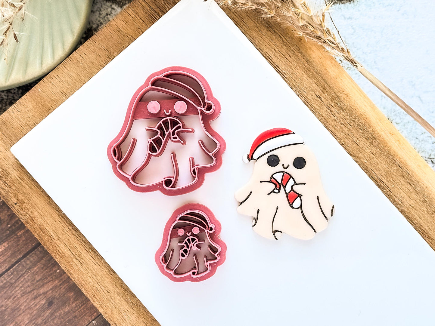 Two spooky Christmas-themed clay cutters and a decorated polymer clay sample. The cutters are pink, ghost-shaped, and wearing Santa hats, holding candy canes.