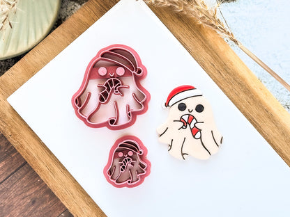Two spooky Christmas-themed clay cutters and a decorated polymer clay sample. The cutters are pink, ghost-shaped, and wearing Santa hats, holding candy canes.