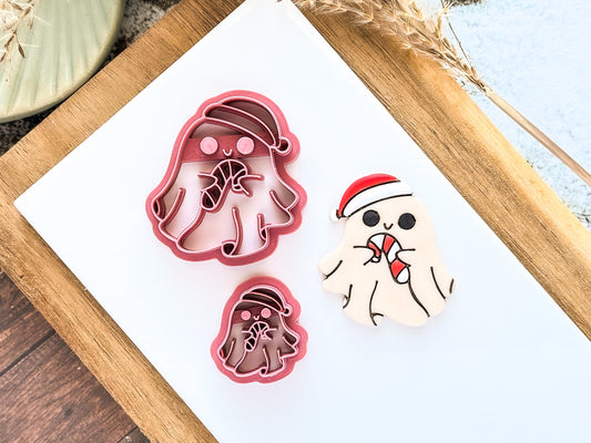 Two spooky Christmas-themed clay cutters and a decorated polymer clay sample. The cutters are pink, ghost-shaped, and wearing Santa hats, holding candy canes.