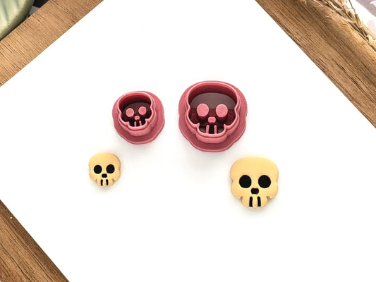2 small skull shaped clay cutters on a white clay baking tile with cut-out samples of polymer clay.