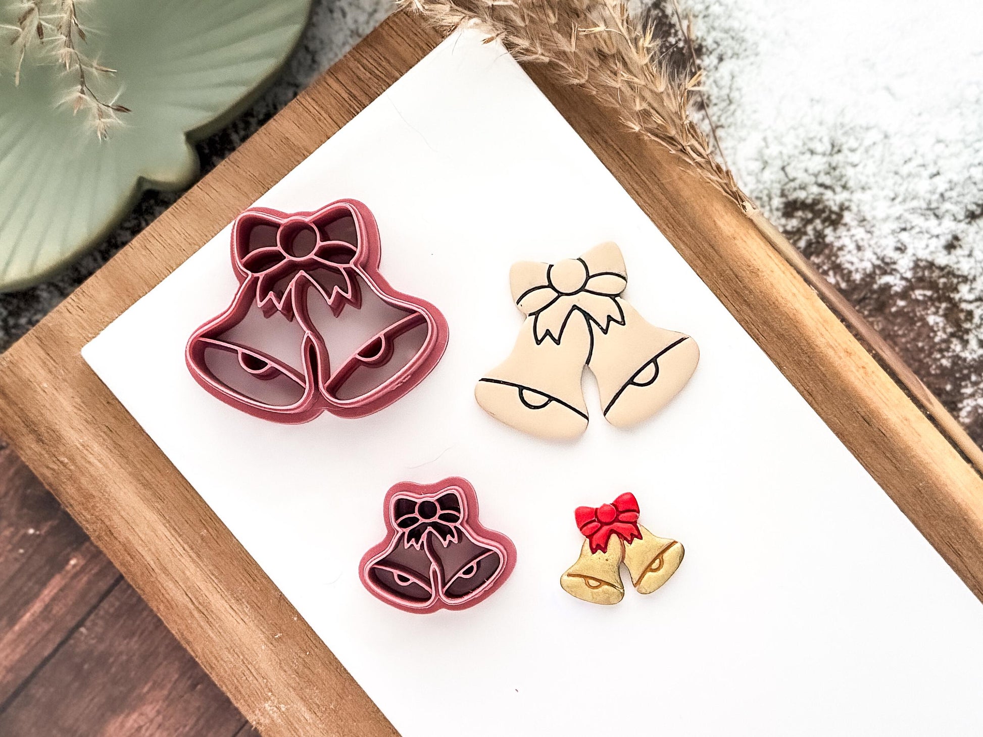 Pink christmas double bell with imprint detail lines and bow shaped clay cutters on a white tile with sample cut-out pieces made from polymer clay.