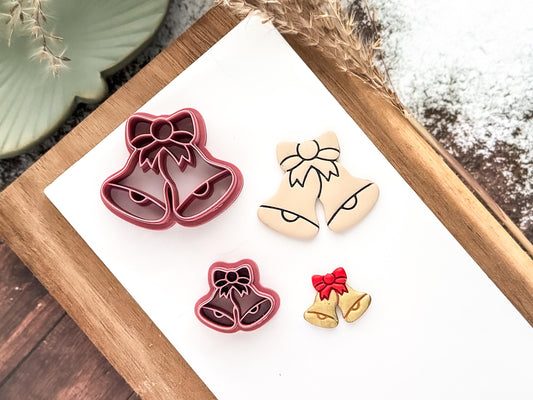 Pink christmas double bell with imprint detail lines and bow shaped clay cutters on a white tile with sample cut-out pieces made from polymer clay.