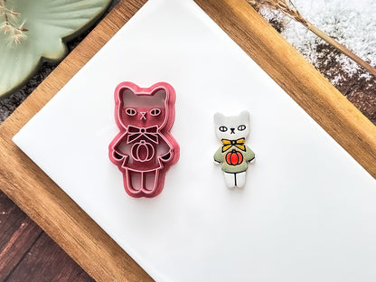 pink cat shaped polymer clay cutter with bow and pumpkin jumper details on a baking tile with a white and green clay cut-out sample.