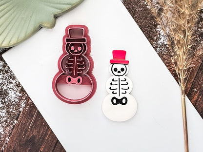 Polymer clay cutter in the shape of a snowman with skeleton details and top hat with a clay cut out sample painted with acrylic paint