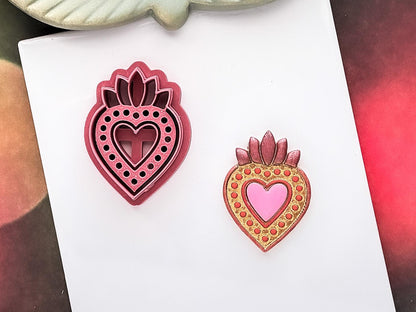 Mexican sacred heart shaped clay cutter for valentines projects and cookie decorations in dark pink. Sample polymer clay cut out painted in acrylic paint in shades of gold and green on a white tile