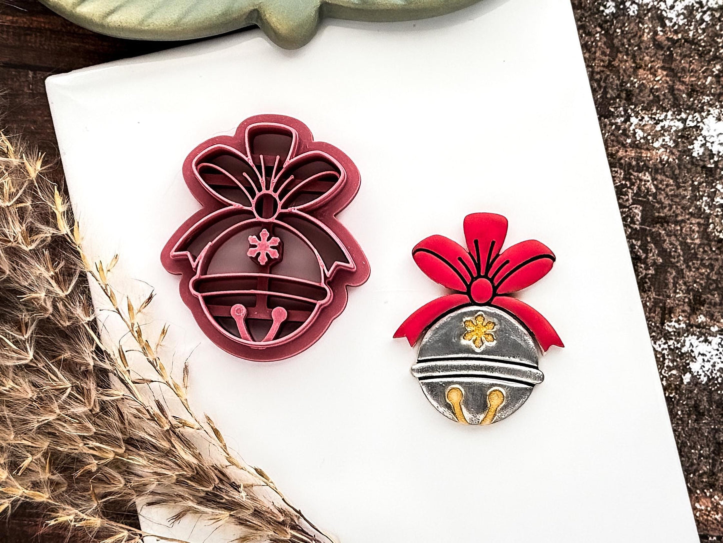 Christmas jingle bell shaped clay cutter in dark pink with polymer clay sample cut out on a white baking tile