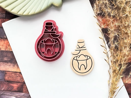 Potion bottle plastic clay cutter with floating tooth and moon details. Polymer clay sample piece next to it on white tile.