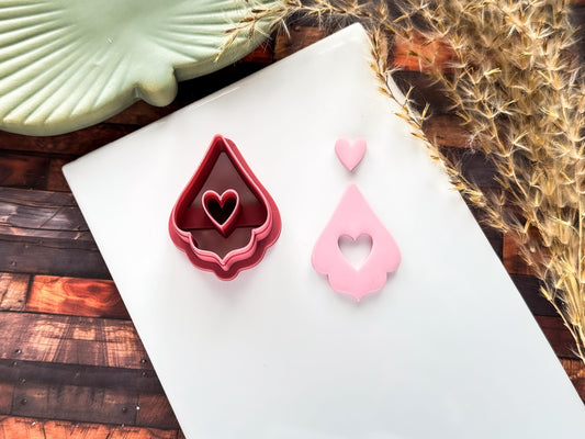 Valetines heart drop clay cutter and polymer clay cut out in pink on a white baking tile.