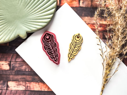 Bohemian peacock feather shaped clay cutter with cut out polymer clay sample on a white tile.