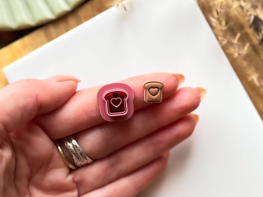 Miniature toast shaped cutter in a hand with a mini toast clay cut out. 